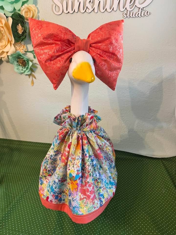 Decorative lawn goose in a floral dress with a large coral bow, studio backdrop with paper flowers