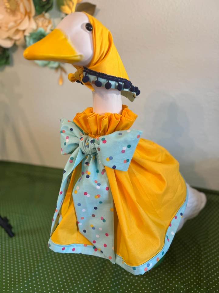 Lawn goose in a bright yellow outfit with teal polka-dot bow and scarf